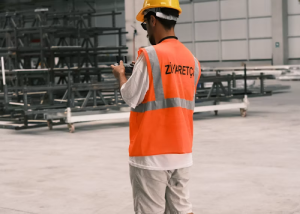 Construction worker in an orange safety vest at a job site, seen from behind